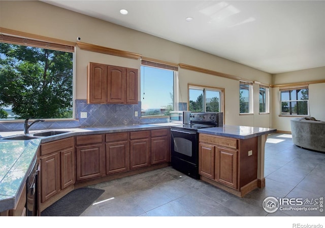 14448 Hanover St, Brighton, CO 80602 - kitchen with black range with electric cooktop, tasteful backsplash, brown cabinetry, a peninsula, and light tile patterned flooring
