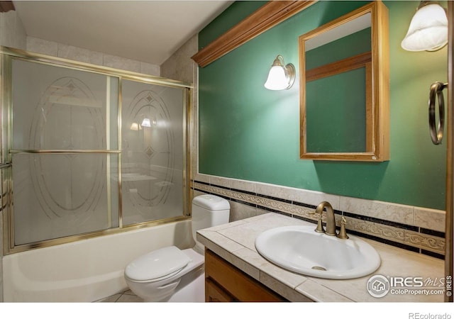 14448 Hanover St, Brighton, CO 80602 - full bath with tile walls, vanity, shower / bath combination with glass door, and a wainscoted wall