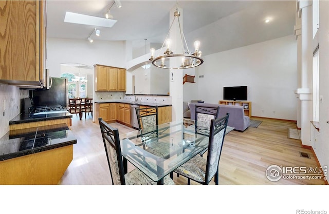 13673 Cook St, Thornton, CO 80602 - dining room featuring a chandelier, rail lighting, light wood-style flooring, high vaulted ceiling, and a skylight