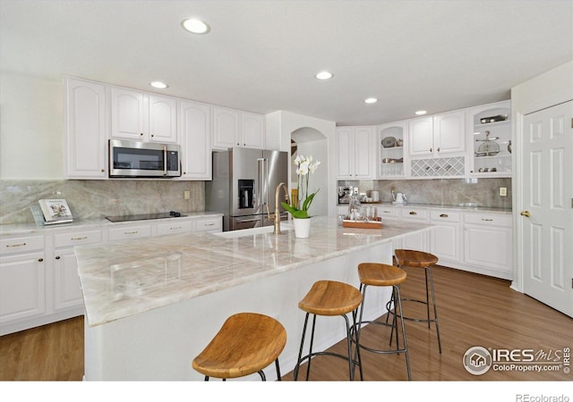 3931 Stonegrass Pt, Broomfield, CO 80023 - kitchen with appliances with stainless steel finishes, open shelves, a breakfast bar area, decorative backsplash, and arched walkways