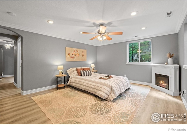 5753 Secrest Ct, Golden, CO 80403 - bedroom featuring light wood-type flooring, ornamental molding, arched walkways, a glass covered fireplace, and ceiling fan
