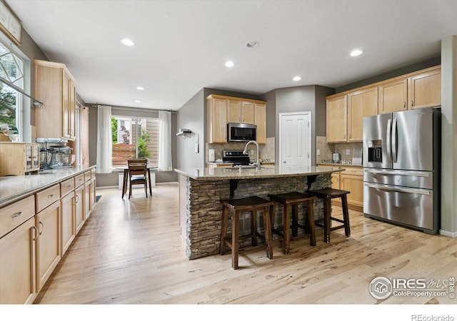 13266 Teller Lake Way, Broomfield, CO 80020 - kitchen featuring stainless steel appliances, light brown cabinetry, light stone counters, light wood-type flooring, and a breakfast bar