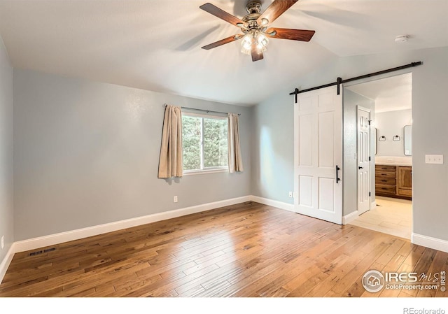 1616 Cedarwood Dr, Longmont, CO 80504 - unfurnished bedroom with a barn door, light wood-style flooring, vaulted ceiling, ensuite bath, and ceiling fan