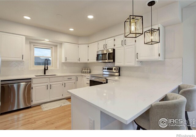 1250 Honeysuckle Ct, Windsor, CO 80550 - kitchen featuring appliances with stainless steel finishes, a peninsula, light wood-type flooring, a kitchen bar, and light countertops