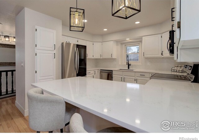 1250 Honeysuckle Ct, Windsor, CO 80550 - kitchen with appliances with stainless steel finishes, a peninsula, light wood-style floors, white cabinetry, and light countertops
