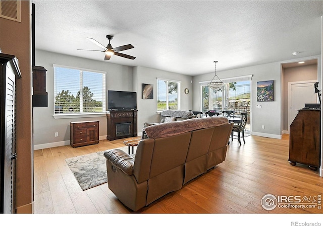 1101 Hillside Ln, Louisville, CO 80027 - living room featuring ceiling fan, light wood-style floors, healthy amount of natural light, a glass covered fireplace, and a textured ceiling