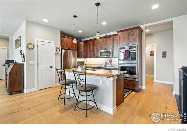 1101 Hillside Ln, Louisville, CO 80027 - kitchen featuring stainless steel appliances, a kitchen breakfast bar, light wood finished floors, hanging light fixtures, and a kitchen island with sink