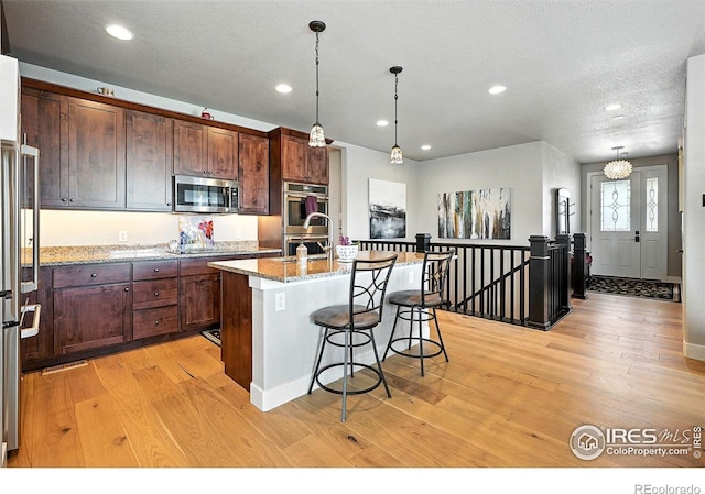 1101 Hillside Ln, Louisville, CO 80027 - kitchen featuring appliances with stainless steel finishes, light wood finished floors, a breakfast bar area, recessed lighting, and an island with sink