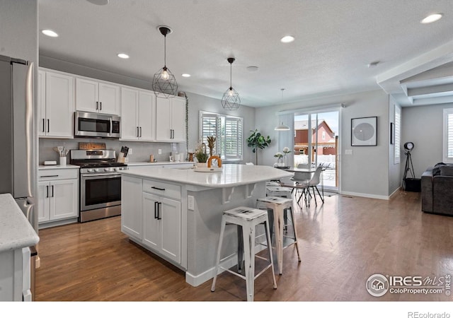 2332 Tabor St, Berthoud, CO 80513 - kitchen featuring stainless steel appliances, wood finished floors, white cabinets, a breakfast bar, and recessed lighting