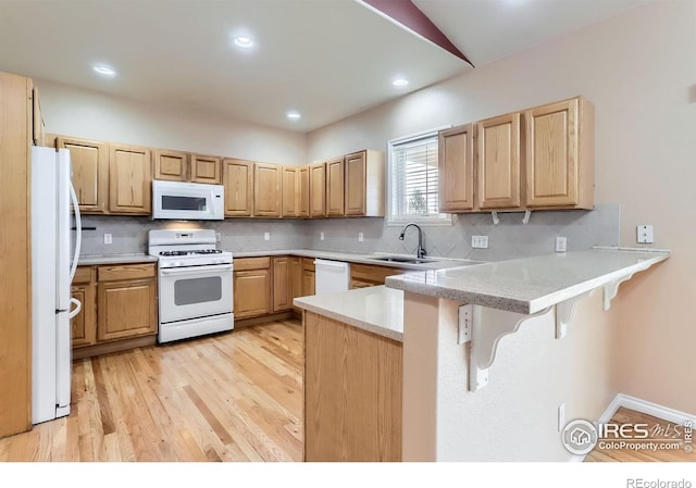 6544 Saddleback Ave, Longmont, CO 80504 - kitchen with white appliances, a peninsula, light wood-type flooring, a kitchen bar, and backsplash