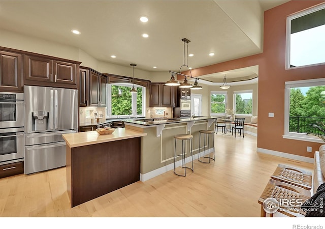 8406 Spinnaker Bay Dr, Windsor, CO 80528 - kitchen with appliances with stainless steel finishes, light wood-type flooring, a spacious island, dark brown cabinets, and a breakfast bar area