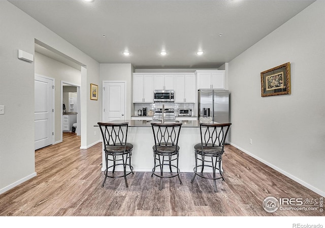 551 Vicot Way Unit D, Fort Collins, CO 80524 - kitchen with stainless steel appliances, a kitchen breakfast bar, wood finished floors, white cabinetry, and a kitchen island with sink