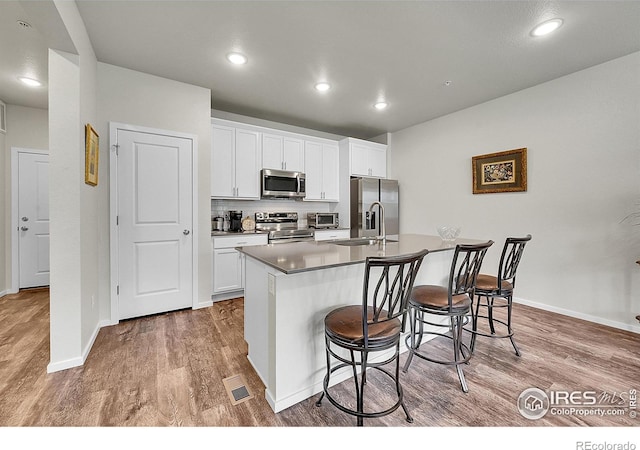 551 Vicot Way Unit D, Fort Collins, CO 80524 - kitchen featuring stainless steel appliances, wood finished floors, a center island with sink, a kitchen bar, and white cabinets
