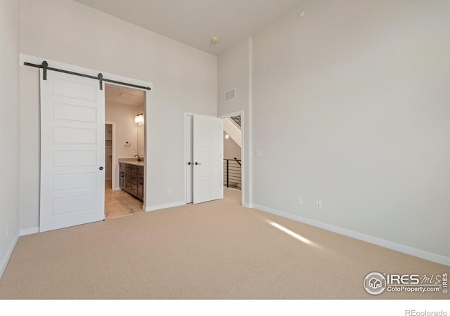 362 Promenade Dr, Superior, CO 80027 - unfurnished bedroom with a barn door, light colored carpet, ensuite bathroom, and a towering ceiling