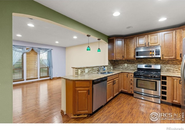 3207 Valmont St, Evans, CO 80620 - kitchen featuring appliances with stainless steel finishes, a peninsula, wood finished floors, backsplash, and recessed lighting