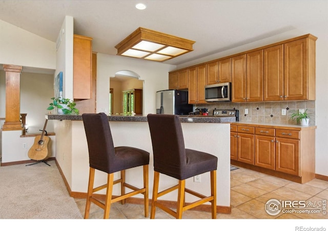 2156 Meander Rd, Windsor, CO 80550 - kitchen with stainless steel microwave, fridge with ice dispenser, a kitchen bar, arched walkways, and brown cabinetry