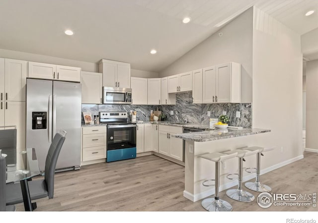 875 E 78th Ave Unit 53, Denver, CO 80229 - kitchen with appliances with stainless steel finishes, a peninsula, decorative backsplash, white cabinetry, and vaulted ceiling