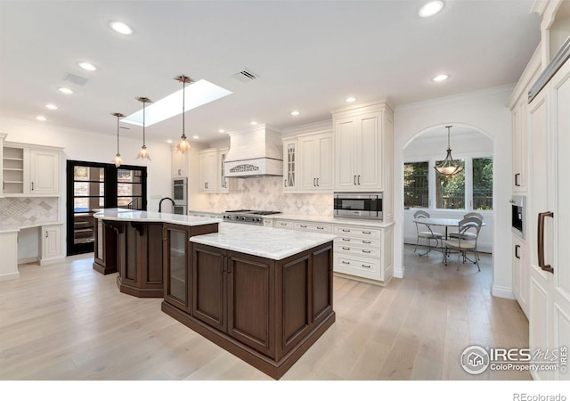 2111 E Alameda Ave, Denver, CO 80209 - kitchen featuring custom exhaust hood, stainless steel microwave, decorative backsplash, open shelves, and light wood finished floors