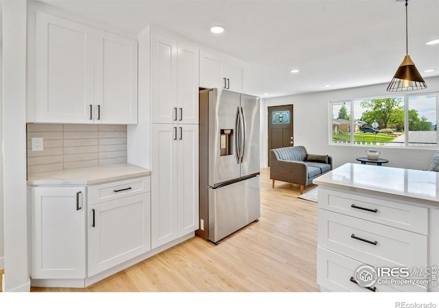 7826 Joan Dr, Denver, CO 80221 - kitchen featuring stainless steel fridge with ice dispenser, light wood finished floors, white cabinetry, tasteful backsplash, and decorative light fixtures