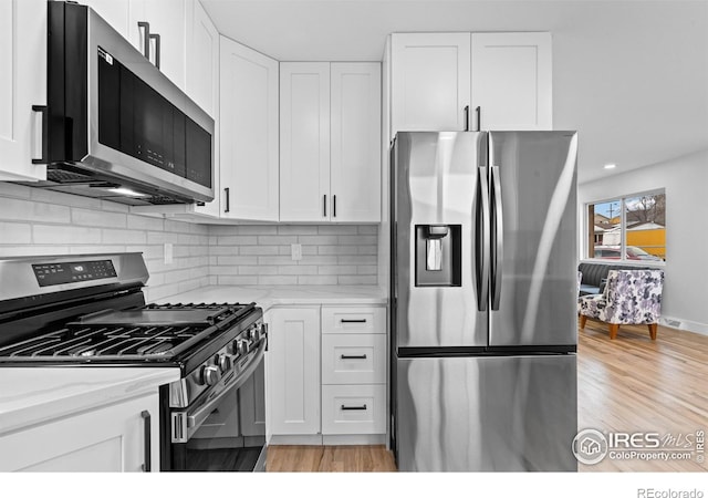9230 Aspen Dr, Thornton, CO 80229 - kitchen featuring stainless steel appliances, white cabinetry, light stone countertops, tasteful backsplash, and light wood finished floors