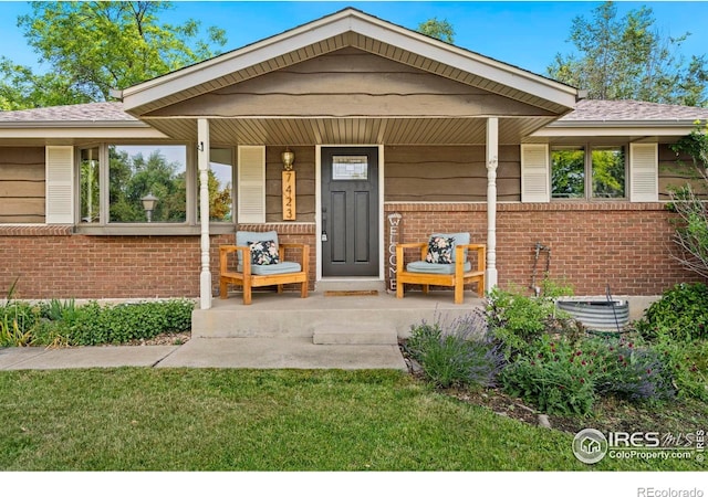 7423 Saulsbury St, Arvada, CO 80003 - view of exterior entry featuring brick siding, covered porch, and a yard