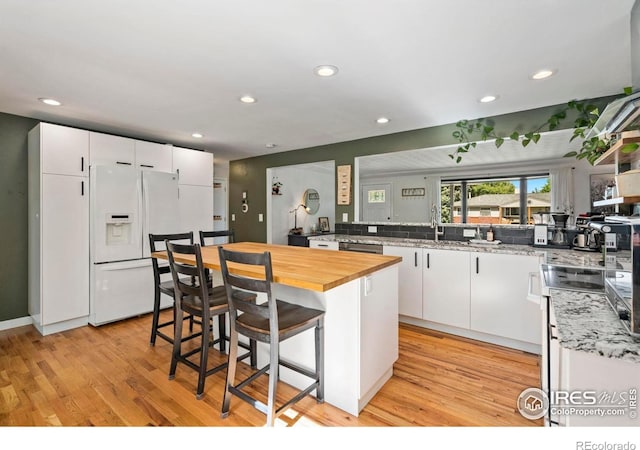 7423 Saulsbury St, Arvada, CO 80003 - kitchen with white fridge with ice dispenser, wood counters, a kitchen bar, white cabinetry, and recessed lighting