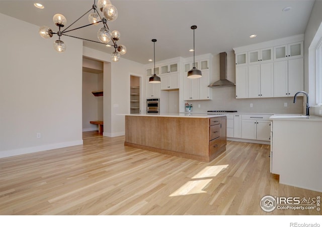 961 Eldorado Ln, Louisville, CO 80027 - kitchen with wall chimney exhaust hood, light wood-type flooring, cooktop, white cabinets, and a center island
