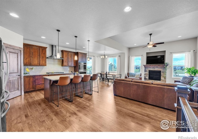 1897 Holloway Dr, Windsor, CO 80550 - kitchen featuring wall chimney range hood, open floor plan, appliances with stainless steel finishes, a breakfast bar, and plenty of natural light