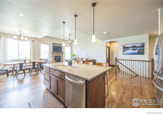 1897 Holloway Dr, Windsor, CO 80550 - kitchen featuring appliances with stainless steel finishes, a fireplace, wood finished floors, a breakfast bar area, and decorative light fixtures