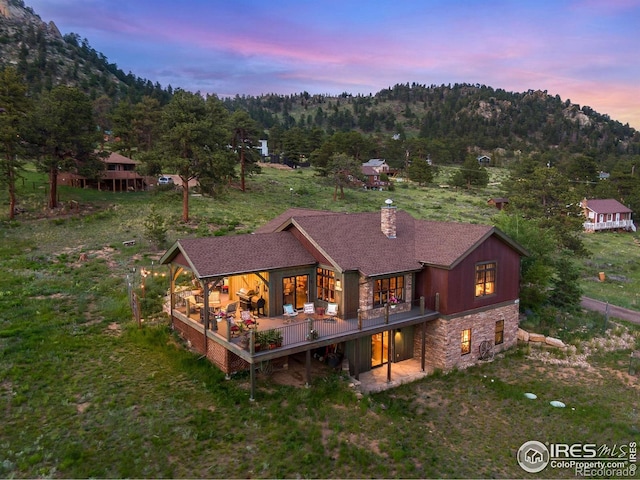 2055 Siskin Dr, Estes Park, CO 80517 - back of property with stone siding, a chimney, a wooden deck, and a forest view