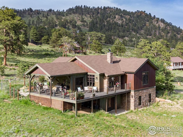 2055 Siskin Dr, Estes Park, CO 80517 - back of house featuring stone siding, a chimney, a lawn, a view of trees, and a deck