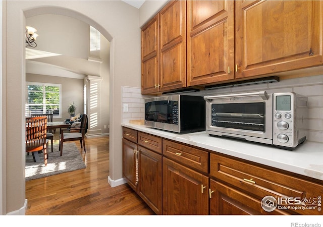 6582 Spanish Bay Dr, Windsor, CO 80550 - kitchen featuring stainless steel microwave, light wood-style flooring, brown cabinets, backsplash, and light countertops