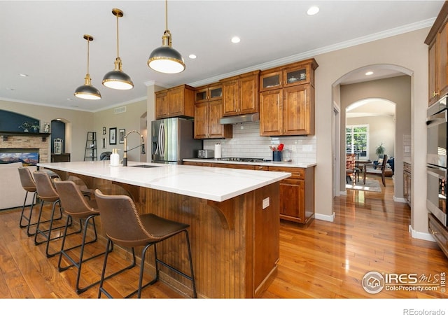 6582 Spanish Bay Dr, Windsor, CO 80550 - kitchen featuring appliances with stainless steel finishes, under cabinet range hood, brown cabinetry, light wood-style flooring, and tasteful backsplash