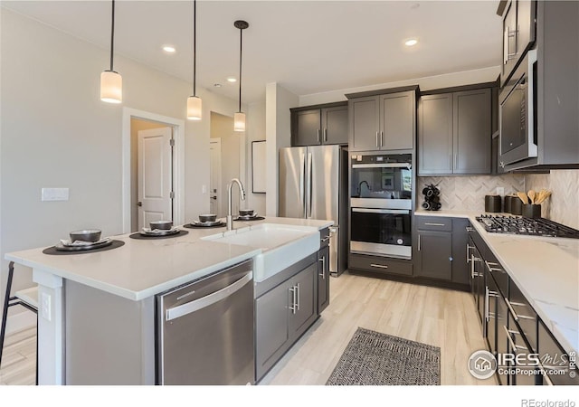 2770 Bear Springs Cir, Longmont, CO 80503 - kitchen with stainless steel appliances, decorative backsplash, hanging light fixtures, a center island with sink, and light wood-style floors