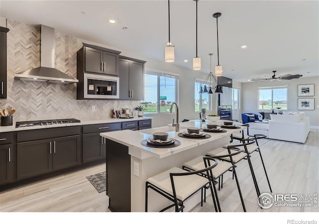 2770 Bear Springs Cir, Longmont, CO 80503 - kitchen featuring wall chimney range hood, appliances with stainless steel finishes, open floor plan, backsplash, and decorative light fixtures