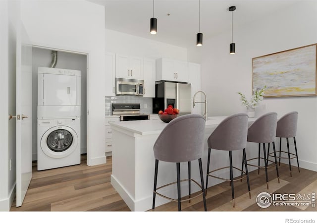 3100 Huron St Unit 1D, Denver, CO 80202 - kitchen with appliances with stainless steel finishes, estacked washer and dryer, a breakfast bar, light wood finished floors, and white cabinetry