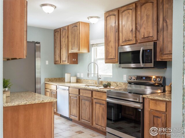1750 Trenton St, Denver, CO 80220 - kitchen featuring appliances with stainless steel finishes, brown cabinets, and light stone counters