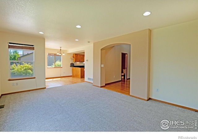 3268 White Buffalo Dr, Wellington, CO 80549 - unfurnished living room with light carpet, a chandelier, arched walkways, and recessed lighting