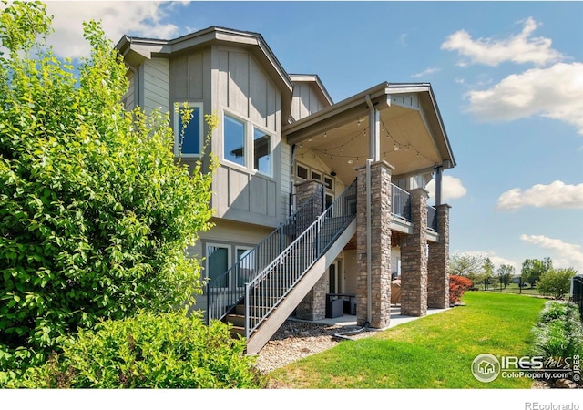 5954 Black Lion Ct, Windsor, CO 80550 - back of property featuring board and batten siding, a lawn, stairs, and stone siding