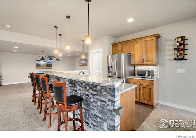5954 Black Lion Ct, Windsor, CO 80550 - kitchen with stainless steel appliances, a large island, hanging light fixtures, brown cabinets, and recessed lighting