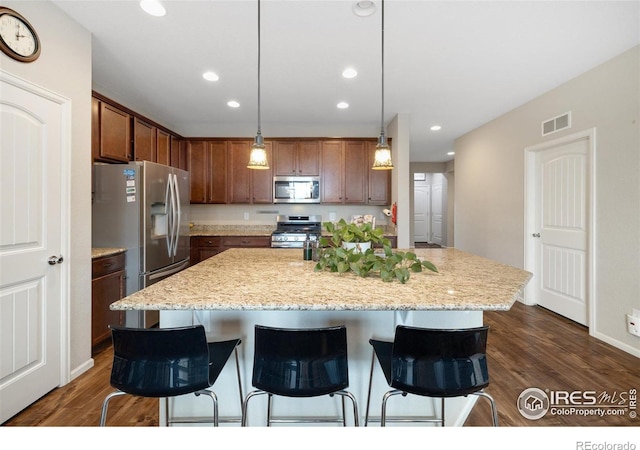 4822 Wildflower Pl, Dacono, CO 80514 - kitchen with appliances with stainless steel finishes, a kitchen bar, recessed lighting, dark wood-type flooring, and a kitchen island