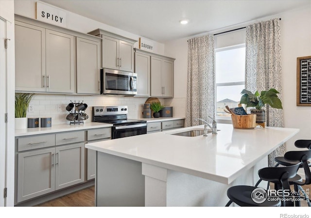 13804 Quartz St, Mead, CO 80504 - kitchen with gray cabinetry, stainless steel appliances, a kitchen breakfast bar, decorative backsplash, and recessed lighting