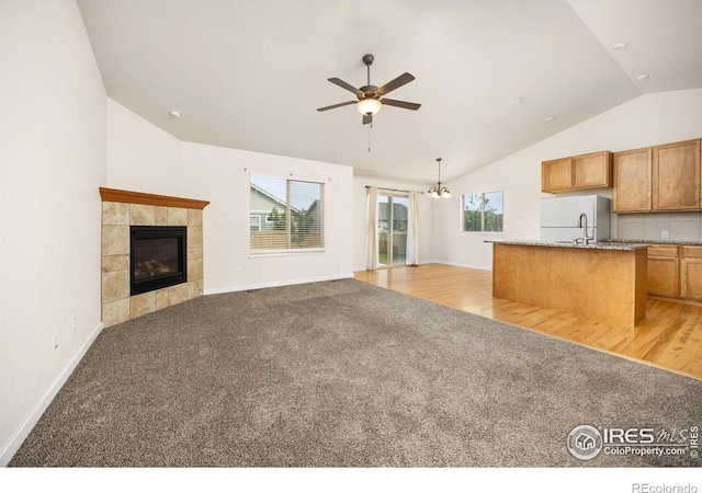 6818 Meadow Rain Way, Wellington, CO 80549 - kitchen featuring light colored carpet, vaulted ceiling, a ceiling fan, open floor plan, and a fireplace