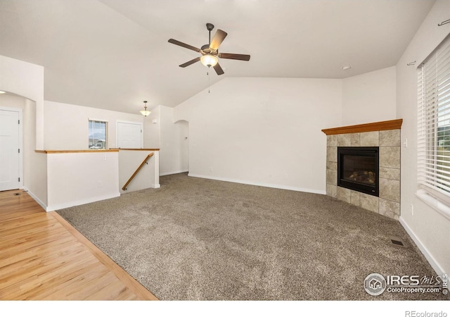 6818 Meadow Rain Way, Wellington, CO 80549 - unfurnished living room with arched walkways, a tiled fireplace, a ceiling fan, lofted ceiling, and carpet flooring