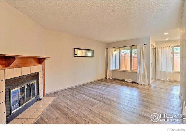 3405 W 16th St Unit 30, Greeley, CO 80634 - unfurnished living room featuring light wood-type flooring, a tiled fireplace, a textured ceiling, and recessed lighting