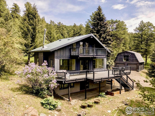 781 Cold Springs Rd, Nederland, CO 80466 - back of property with a garage, an outdoor structure, a wooden deck, a wooded view, and board and batten siding