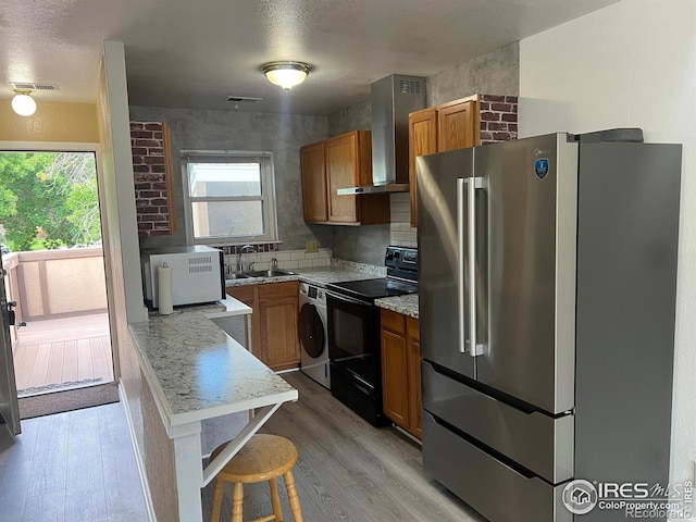 225 E 8th Ave Unit B11, Longmont, CO 80504 - kitchen featuring freestanding refrigerator, black range with electric cooktop, wall chimney exhaust hood, brown cabinetry, and washer / dryer