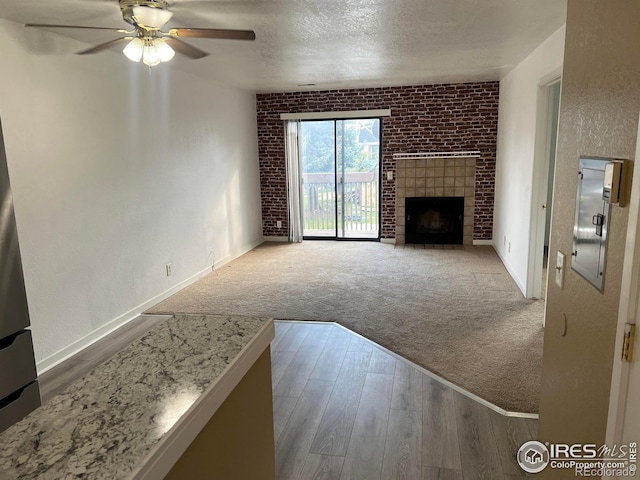 225 E 8th Ave Unit B11, Longmont, CO 80504 - unfurnished living room with a ceiling fan, carpet floors, a brick fireplace, wood finished floors, and a textured ceiling