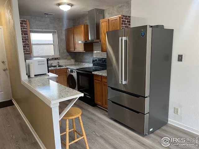 225 E 8th Ave Unit B11, Longmont, CO 80504 - kitchen with freestanding refrigerator, black electric range oven, wall chimney range hood, washer / dryer, and light wood-style floors