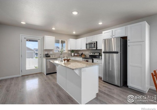 4216 Yellowbells Dr, Evans, CO 80620 - kitchen with appliances with stainless steel finishes, light wood finished floors, white cabinetry, a kitchen island, and recessed lighting
